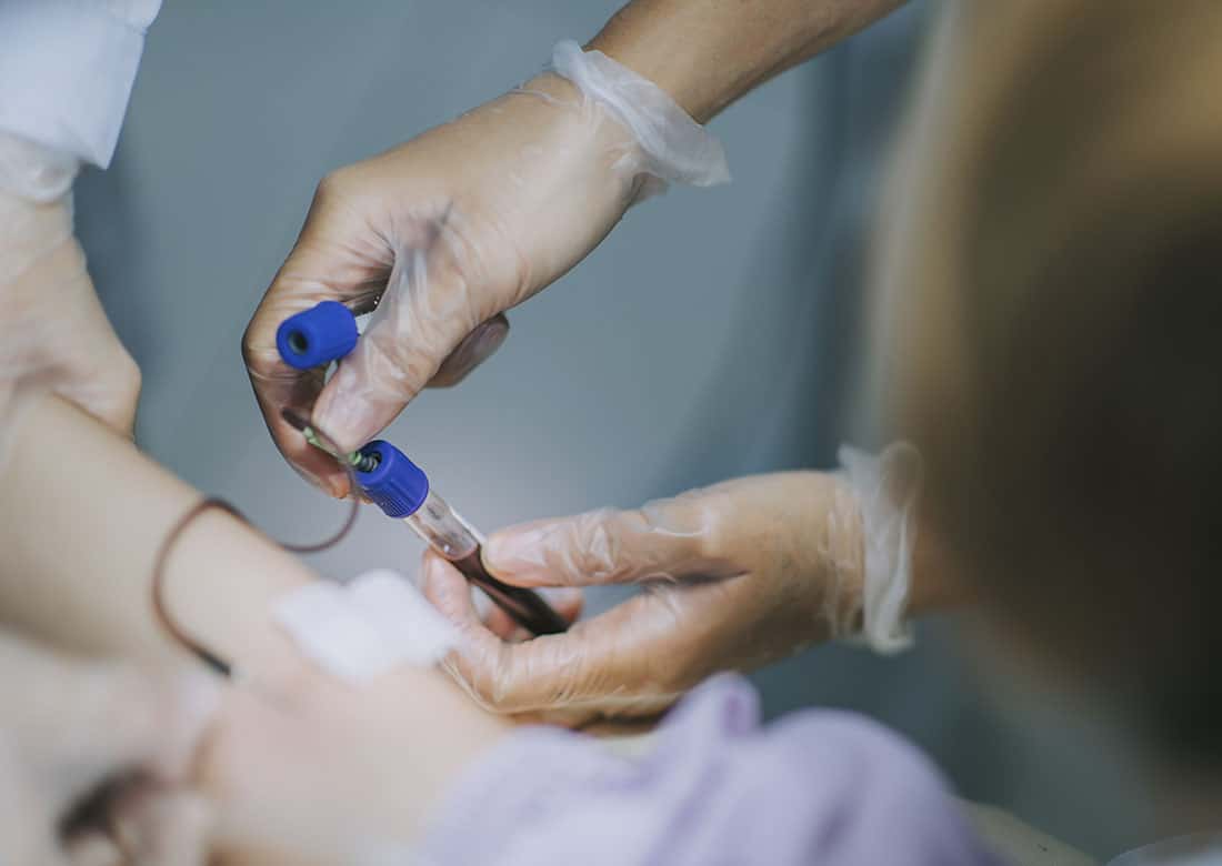 close up asian chinese nurse drawing blood from female chinese patient arm's vein in the clinic